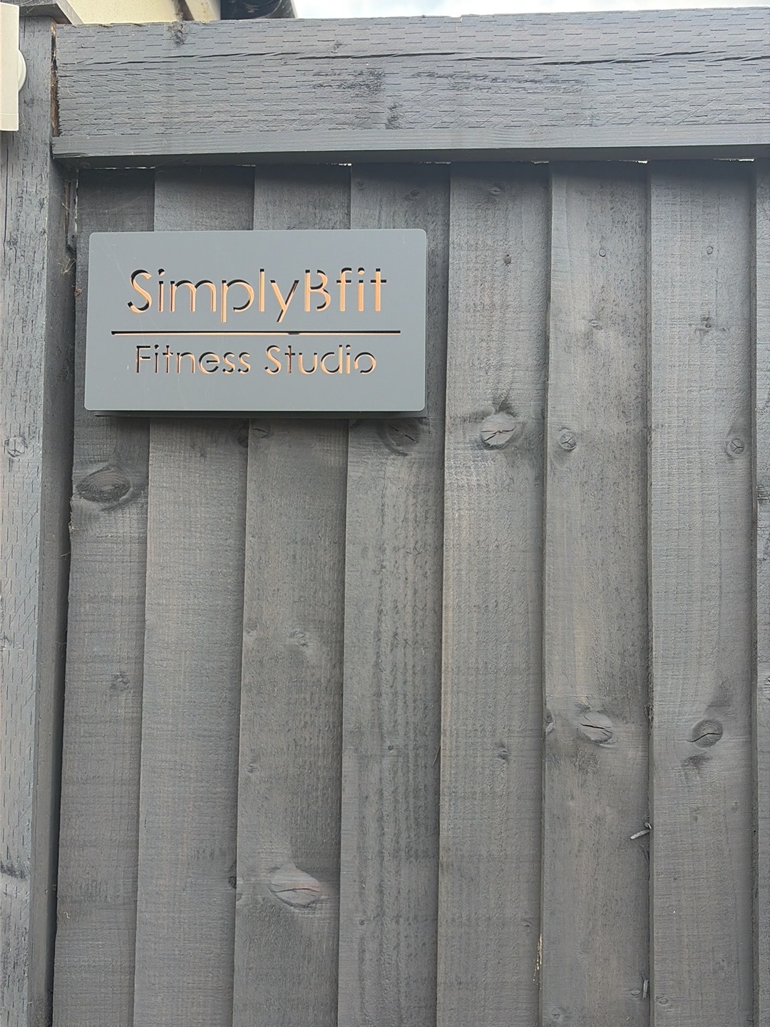 The SimplyBfit Fitness Studio sign on a dark timber fence
