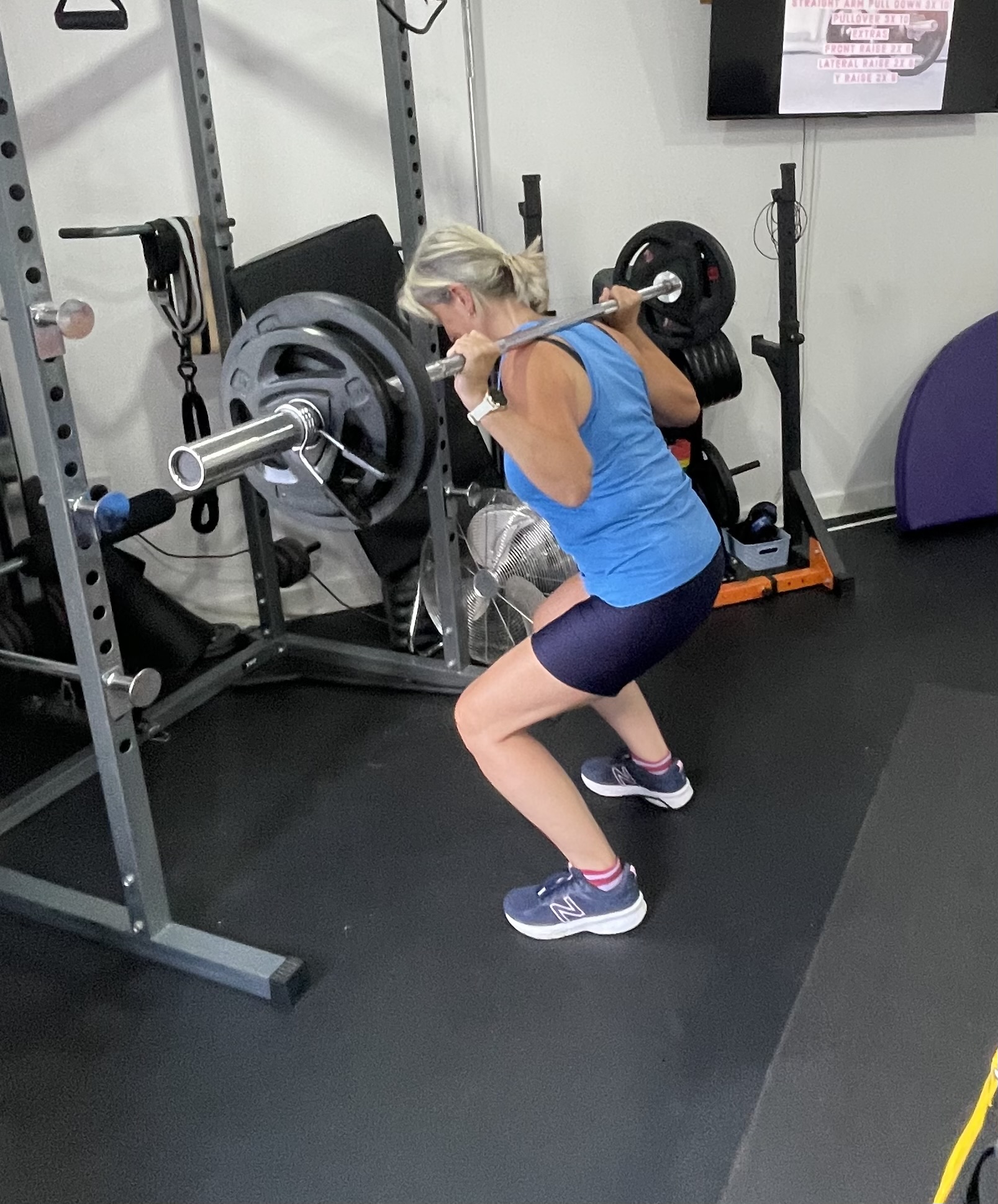 A member squatting with a barbell in the rack
